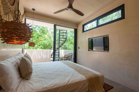 Elegant bedroom with a cozy boho design, king-size bed a wall-mounted TV, and warm rattan lighting. A balcony features a spiral staircase leading up to a private rooftop terrace.