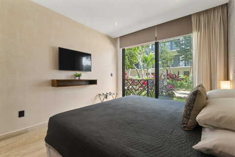 This chic bedroom features a king-size bed with decorative macramé, a wall-mounted TV, and access to a private balcony overlooking lush greenery. Perfect for relaxation and comfort.