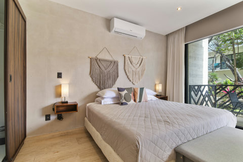 This serene bedroom features cozy wall hangings, a comfy bed with modern linens, and a large window with a view of lush greenery, complemented by soft lighting and a minimalistic design.