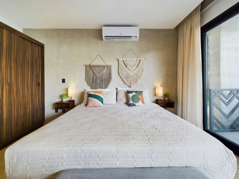 King bed with soft bedding, boho macramé decor, and stylish pillows and AC. Warm lighting and floor-to-ceiling windows create a bright, cozy, and modern retreat for a relaxing stay.