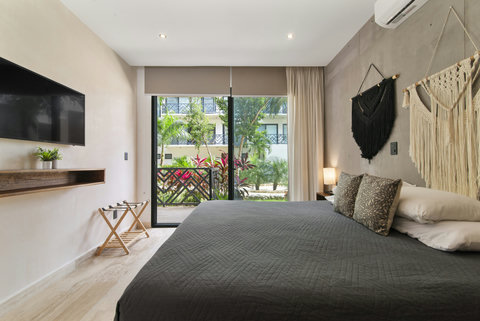 Unwind in a chic bedroom with a king-size bed, boho macramé accents, and a wall-mounted TV. Step onto your private balcony and enjoy peaceful views of lush greenery.
