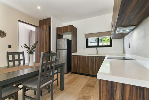 This stylish kitchen with sleek wooden cabinetry, a modern refrigerator, and elegant countertops is complemented by a simple dining area, perfect for relaxing or enjoying meals.