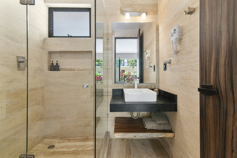 This sleek, modern bathroom features a walk-in shower with glass doors, a stylish vessel sink, and natural stone finishes. Large windows offer natural light and a view of lush greenery outside.