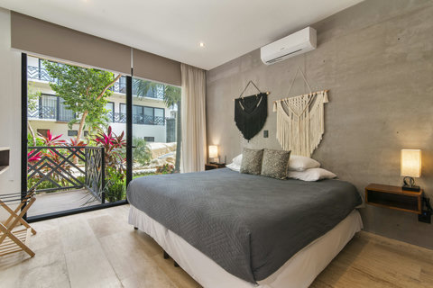 This stylish bedroom features a cozy king-size bed, modern macramé wall art, and a beautiful garden view through floor-to-ceiling windows. A perfect retreat with air conditioning for comfort.