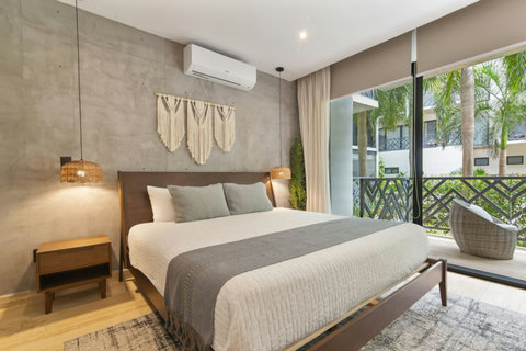 Rest easy in this stylish bedroom featuring a king bed, soft lighting, boho-chic décor, and floor-to-ceiling windows with views of lush tropical gardens.