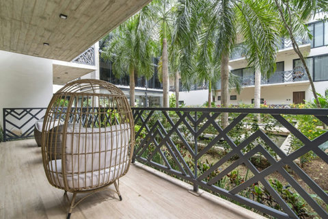 Relax in a cozy rattan egg chair on this tropical terrace, surrounded by lush palm trees, stylish iron railings, and views of the serene shared garden below.