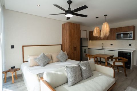 Stylish studio with a comfy bed, sofa, wooden dining set, full kitchenette, fridge, microwave, pendant lights, and ceiling fan—modern comfort with natural touches.