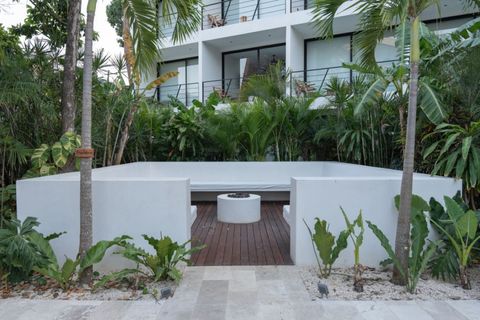 Cozy outdoor lounge with white concrete seating and a central fire pit, surrounded by lush greenery—ideal for evening gatherings or peaceful moments in nature.