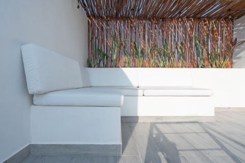 Rooftop lounge with built-in white cushioned seating, wooden privacy screen, and tropical plants—perfect for relaxing under the Tulum sun or stars.