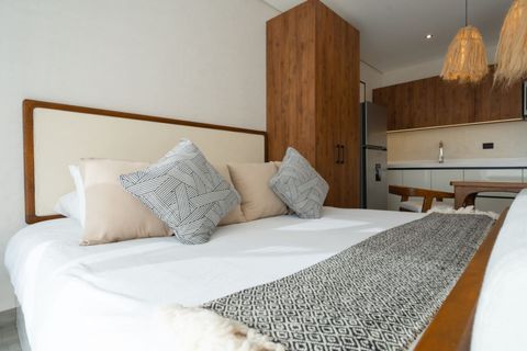 Comfortable king bed with neutral pillows, cozy textures, and a view of the wood-accented wardrobe and modern kitchenette.