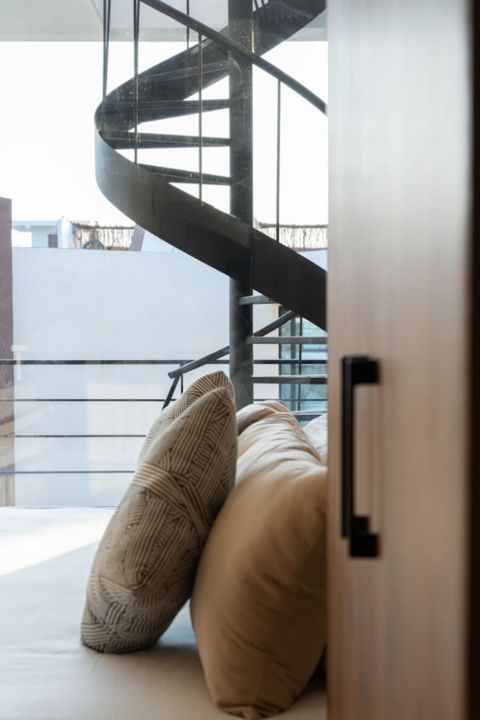 Close-up of cozy pillows on a bed with a sleek spiral staircase leading to the terrace