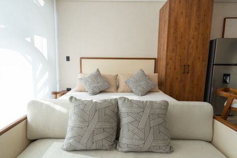 Inviting studio with a cozy bed, cushioned sofa, patterned pillows, wooden wardrobe, and neutral tones for a warm, minimalist vibe.