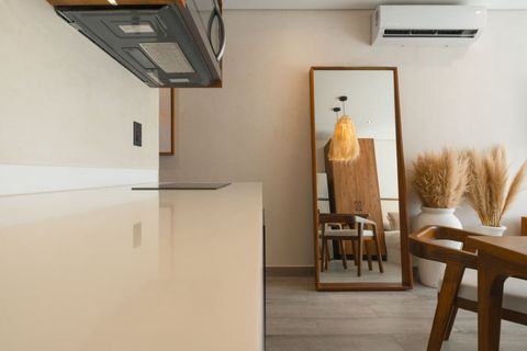 Minimalist kitchen view with a sleek counter, modern appliances, a large wooden-framed mirror, pampas grass in a white vase, and wooden furniture creating a warm, natural ambiance.