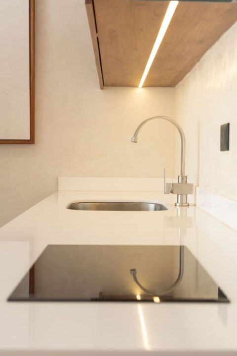 Close-up of a sleek white countertop featuring a modern electric cooktop and a minimalist stainless steel sink, enhanced by warm under-cabinet lighting and wood accents.