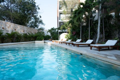 Inviting pool surrounded by lush greenery, stone walls, and wooden sun loungers with cushions. A tranquil spot to relax and enjoy the Tulum sun.