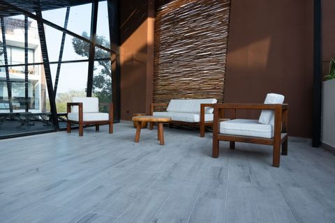 Outdoor lounge with modern wooden furniture and white cushions, set against a natural woven divider and large glass windows, creating a peaceful, stylish space.