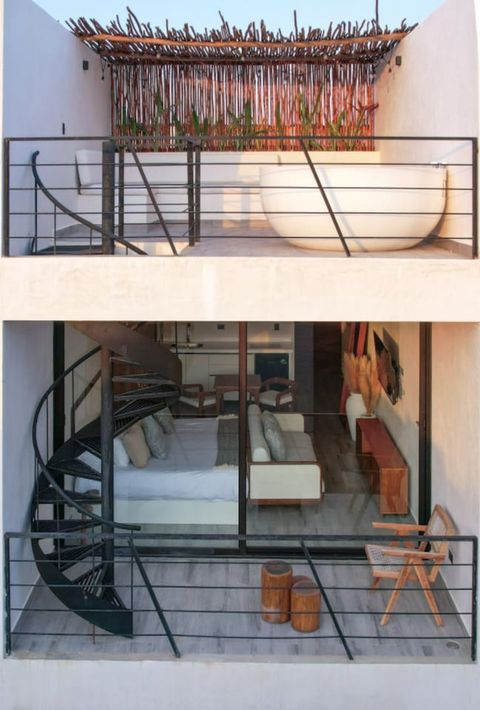 Two-level space with a cozy studio on the lower floor, featuring a spiral staircase leading to a private rooftop terrace with a soaking tub and lush privacy wall.