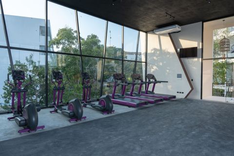 Spacious gym with cardio machines, large floor-to-ceiling windows, and modern design. Natural light and jungle views make workouts energizing and refreshing.