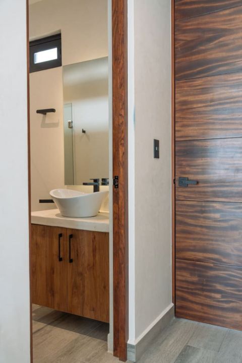 A modern bathroom with a stylish vessel sink, wood vanity, and large mirror, seen through a doorway with warm wood accents and minimalist design.