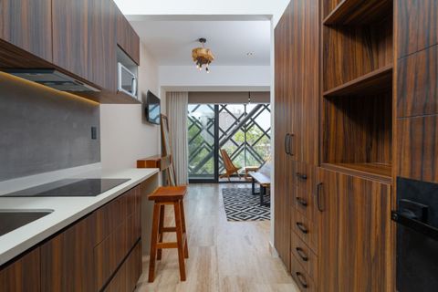 Fully equipped kitchen with induction stove, microwave, bar stool, spacious cabinets, and a balcony with wooden chairs and natural light.