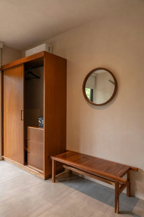 Minimalist wardrobe space. A sleek wooden closet, a round mirror, and a cozy bench provide both style and functionality for a comfortable stay.