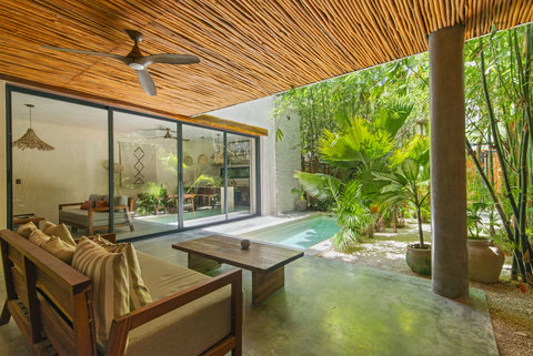 Tropical open-air living space. Features a cozy lounge area with plush seating, a private pool, lush greenery, and a stylish thatched pergola—perfect for relaxation in a serene setting.