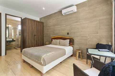 Cozy Tulum bedroom with A/C, private ensuite bathroom, natural wood decor, closet, and a small work/dining space—perfect for comfort, style, and rest after beach adventures!