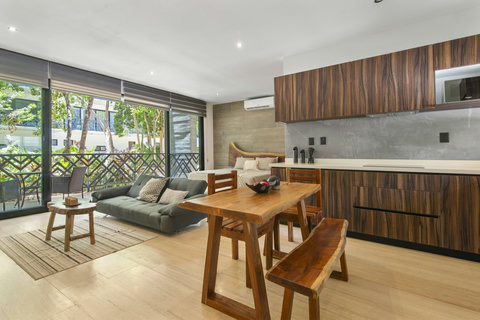 Open-concept layout featuring a modern kitchen, a cozy lounge area, and a dining set—all framed by floor-to-ceiling windows that let in natural light and lush garden views.