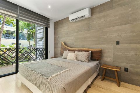 Spacious king bed with artisanal wood headboard, soft bedding, A/C, and natural light from a private garden-facing terrace.
