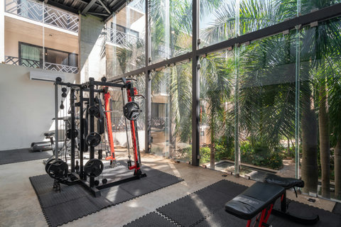 Modern gym with floor-to-ceiling windows and lush views, featuring weights, cardio machines, and space for stretching in a refreshing atmosphere.
