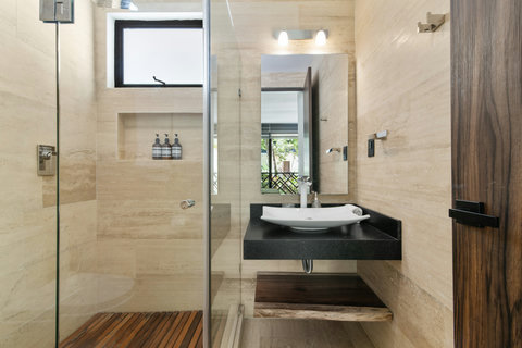 Modern bathroom with sleek stone walls, a glass rain shower, and a designer sink—crafted for comfort, style, and relaxation.