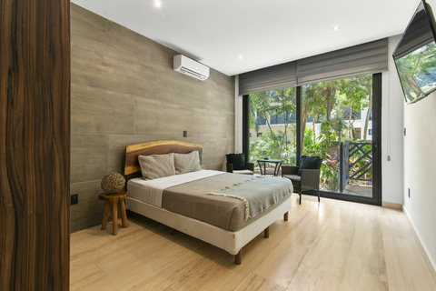 Relax in this serene bedroom featuring a handcrafted wood headboard, plush bedding, A/C, and floor-to-ceiling windows that open to a lush garden-facing terrace.