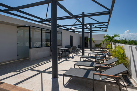 Rooftop terrace with chic lounge chairs and shaded seating—perfect for sunbathing, relaxing with a drink, and enjoying sweeping city and sky views.