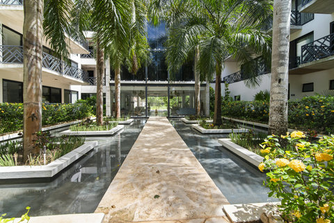 Walk through a serene tropical courtyard with a reflecting pool, lush palm trees, and vibrant flowers. Perfect for guests seeking a peaceful, nature-inspired stay!