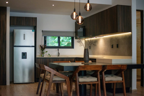 Modern kitchen with wood cabinets, stainless steel fridge, and black dining table. Pendant lights add charm and warmth.