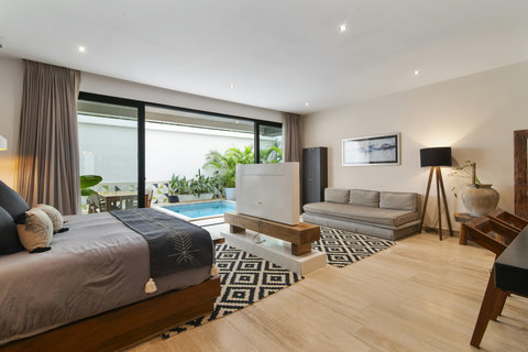 Unwind in a chic bedroom with a modern bed, cozy sofa, and elegant decor. Sliding doors reveal a private pool and garden, with pendant lights and a stylish rug adding charm.