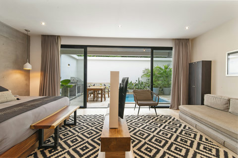 Stylish bedroom with modern bed, cozy sofa & chic decor. Sliding doors open to a private pool and outdoor lounge, with pendant lights and a patterned rug for extra charm.