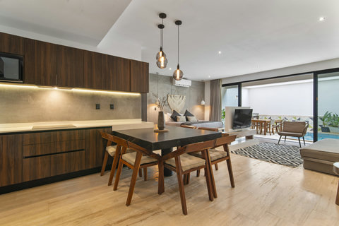 Experience a stylish hotel apartment with a sleek kitchen featuring wooden cabinets and pendant lights. The modern dining area includes a chic table and chairs, while large windows open to a private pool and lush garden