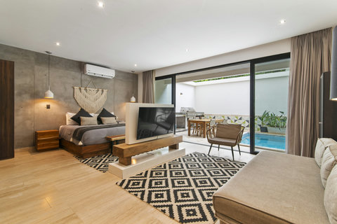 Chic bedroom with modern bed, cozy sofa & stylish decor. Sliding doors lead to a private pool and dining area, with pendant lights and a patterned rug adding warmth.