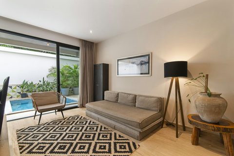 Discover a cozy  room with a modern sofa, stylish chair, and chic rug. Enjoy natural light from large windows opening to a private pool and lush garden. Perfect for a relaxing stay!