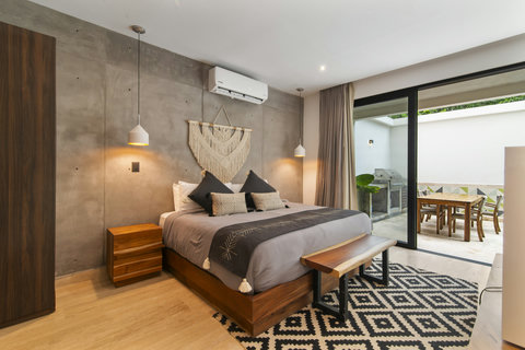 Sleep in style with a modern king  bed, cozy pillows, and warm wood furniture. Sliding doors lead to a private outdoor dining area with pendant lights and a soft rug.