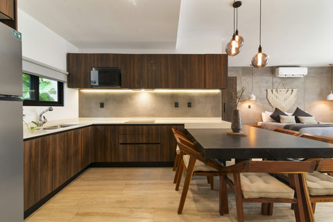 Contemporary kitchen with wood cabinetry, stainless fridge, and a chic black table. Warm lighting and natural light create a cozy, inviting feel.