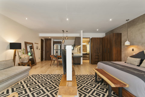 Cozy bedroom with a modern bed and decorative pillows, sleek sofa, and chic dining area. Warm lighting, wood accents, and natural light create a stylish, inviting vibe.