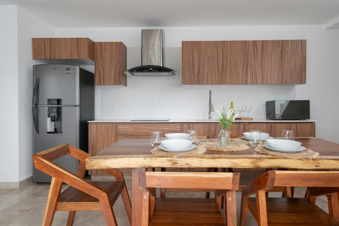 Modern open-concept kitchen featuring elegant wood finishes, premium appliances, and a handcrafted solid wood dining table—ideal for enjoying stylish gatherings and relaxed meals in Tulum.
