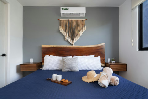 Inviting bedroom with a handcrafted wooden headboard, soft lighting, and boho macramé art. Neutral tones and minimal decor create a calm, relaxing space ideal for unwinding after a beach day.