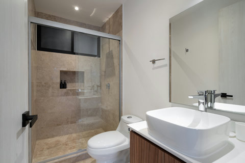 Elegant bathroom featuring a glass shower, warm beige tiles, and natural light that enhances its airy feel. The bedroom view and ceiling fan add a fresh, spa-like touch to the space.