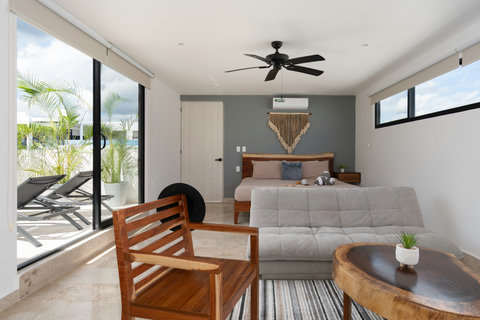 Bright third bedroom featuring a king-size bed, sofa bed, A/C, Smart TV, and private patio with lush plants and a lounge chair—perfect for relaxing or enjoying a quiet morning coffee.