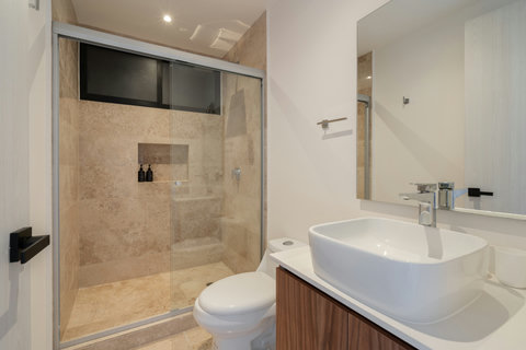 Stylish second bathroom with glass shower, beige tiles, and soft natural light. The view from the bedroom and ceiling fan combine to create a serene, spa-inspired atmosphere.