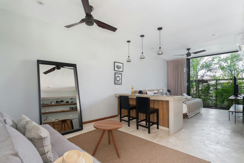 A stylish studio layout featuring a cozy living area, a spacious dining island, and calming views of tropical plants. It’s a refreshing, inviting space designed to make your stay comfortable and relaxing.