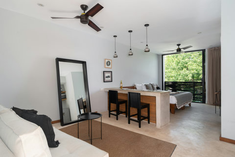 Enjoy a stylish studio featuring a comfortable living area, a spacious dining island, and calming views of tropical plants. A bright, refreshing space designed for relaxation and ease.